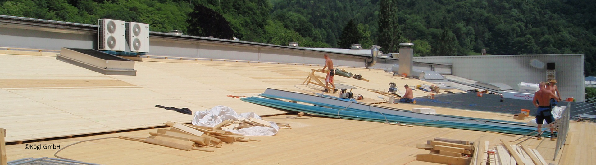 großes Dach mit Holzschalung, in der Mitte liegen Blechbahnen, die auf der rechten Seite eingedeckt werden